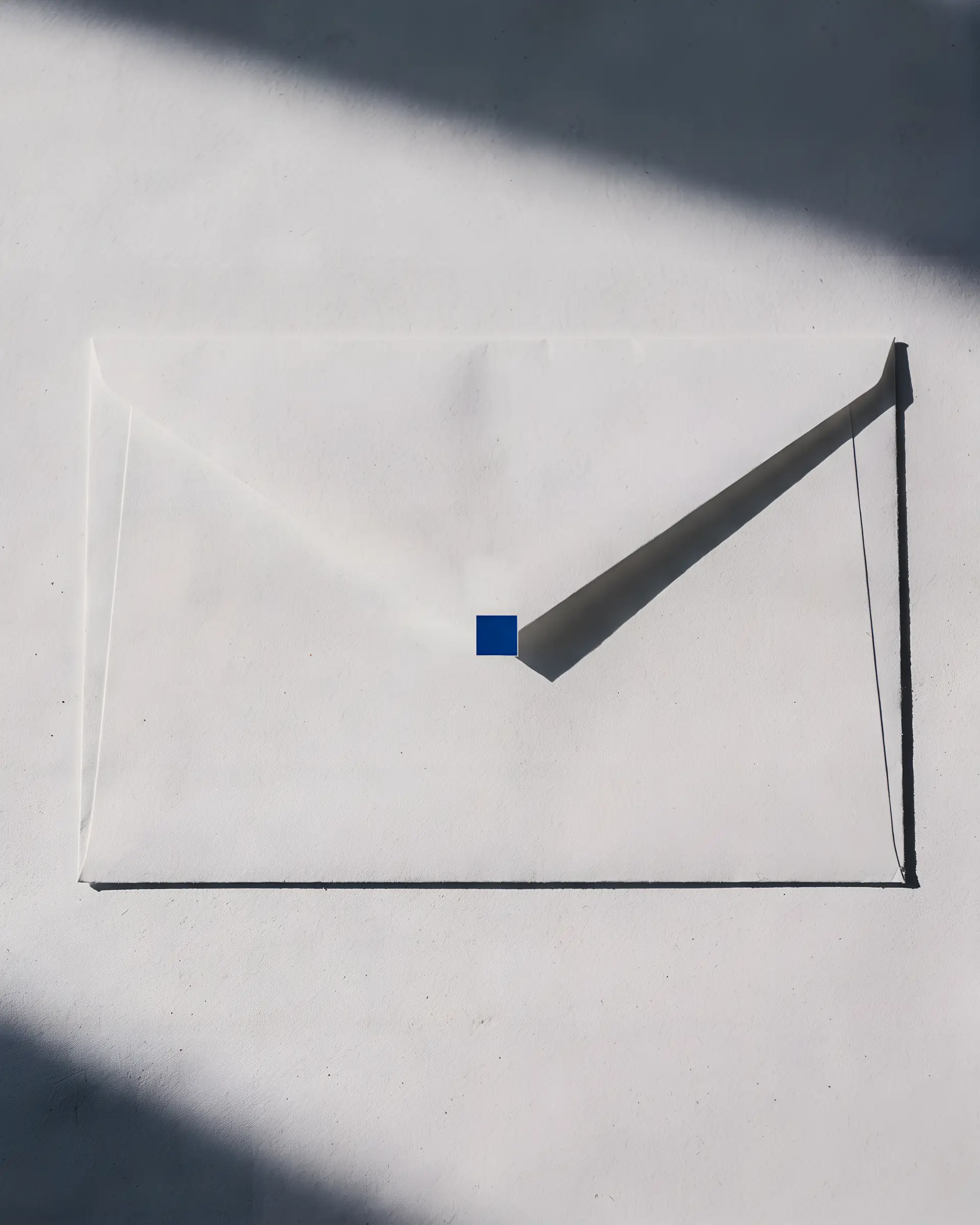 A plain envelope on a pale surface, a small blue square sealing the point of its flap.