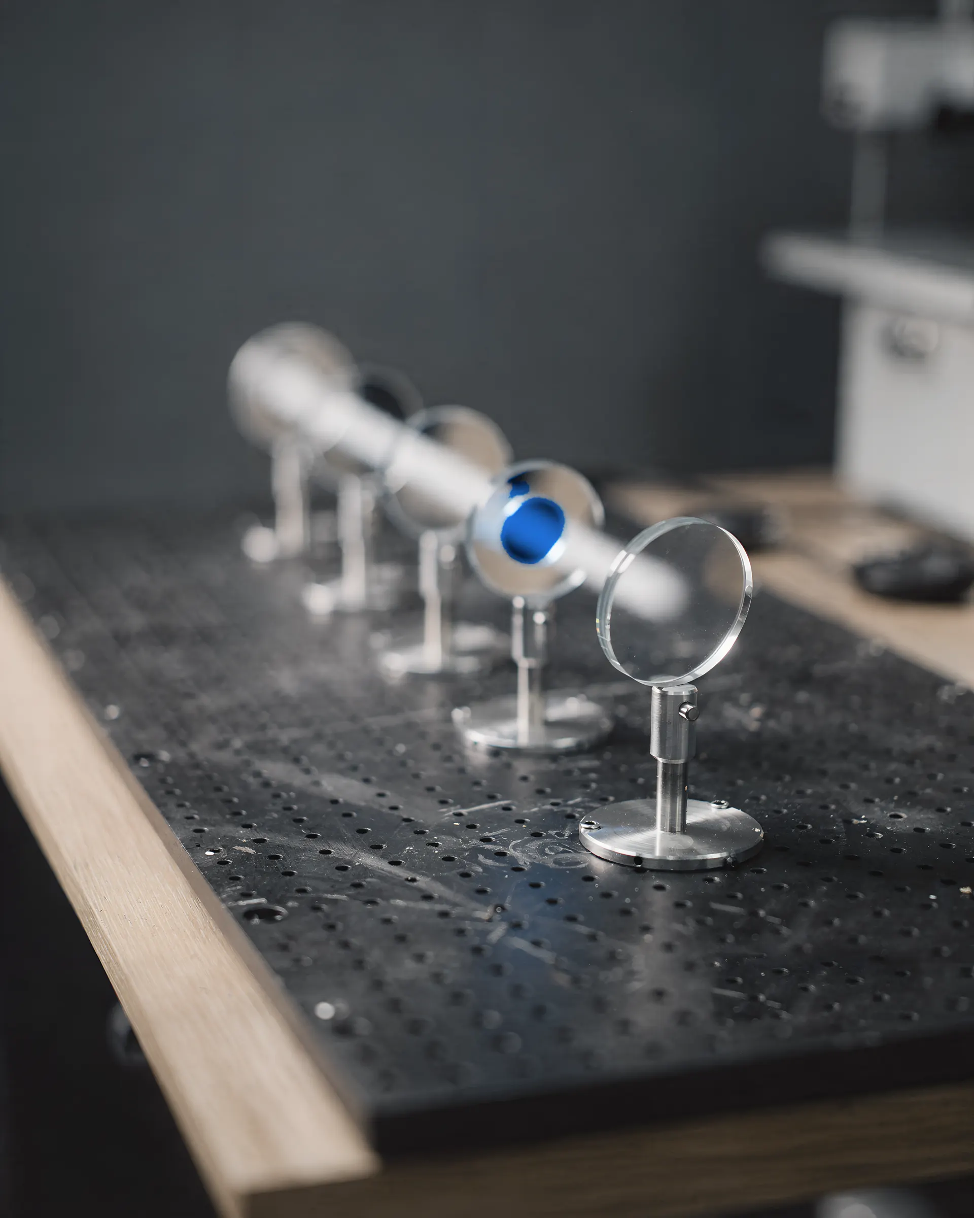 A soft path of light passing through a row of mounted lenses and one blue filter on an optical breadboard.